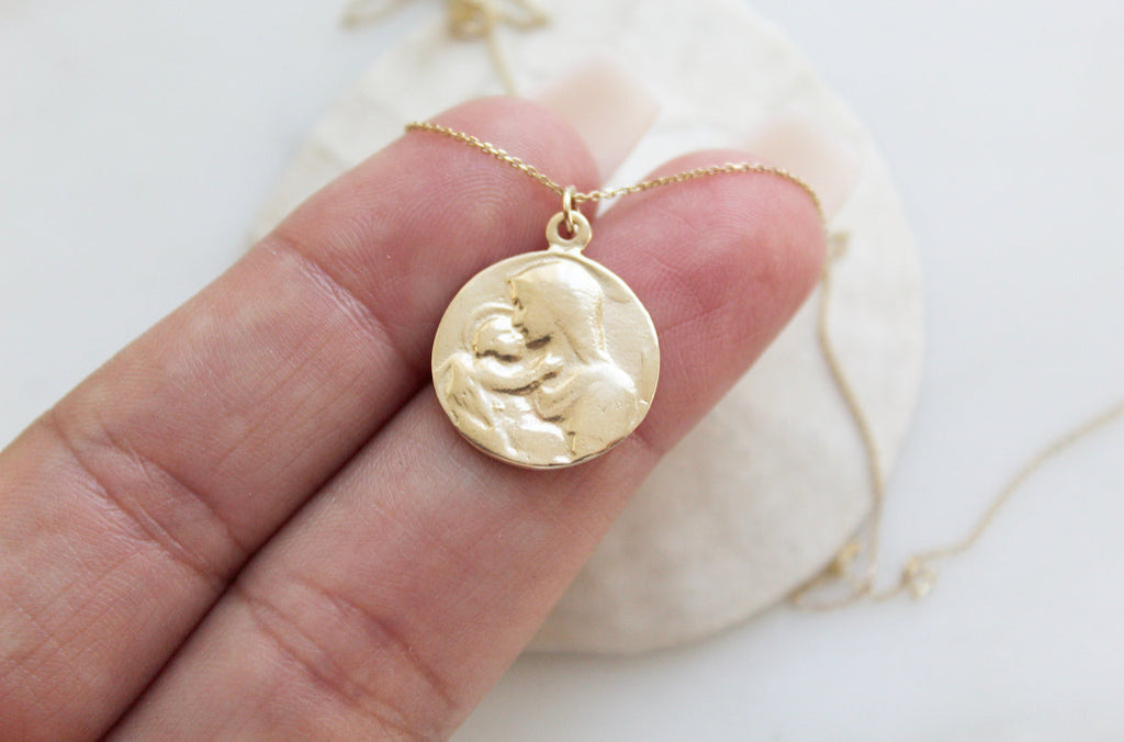 14k gold medallion pendant necklace with Jesus and Mary relief, angled view in palm