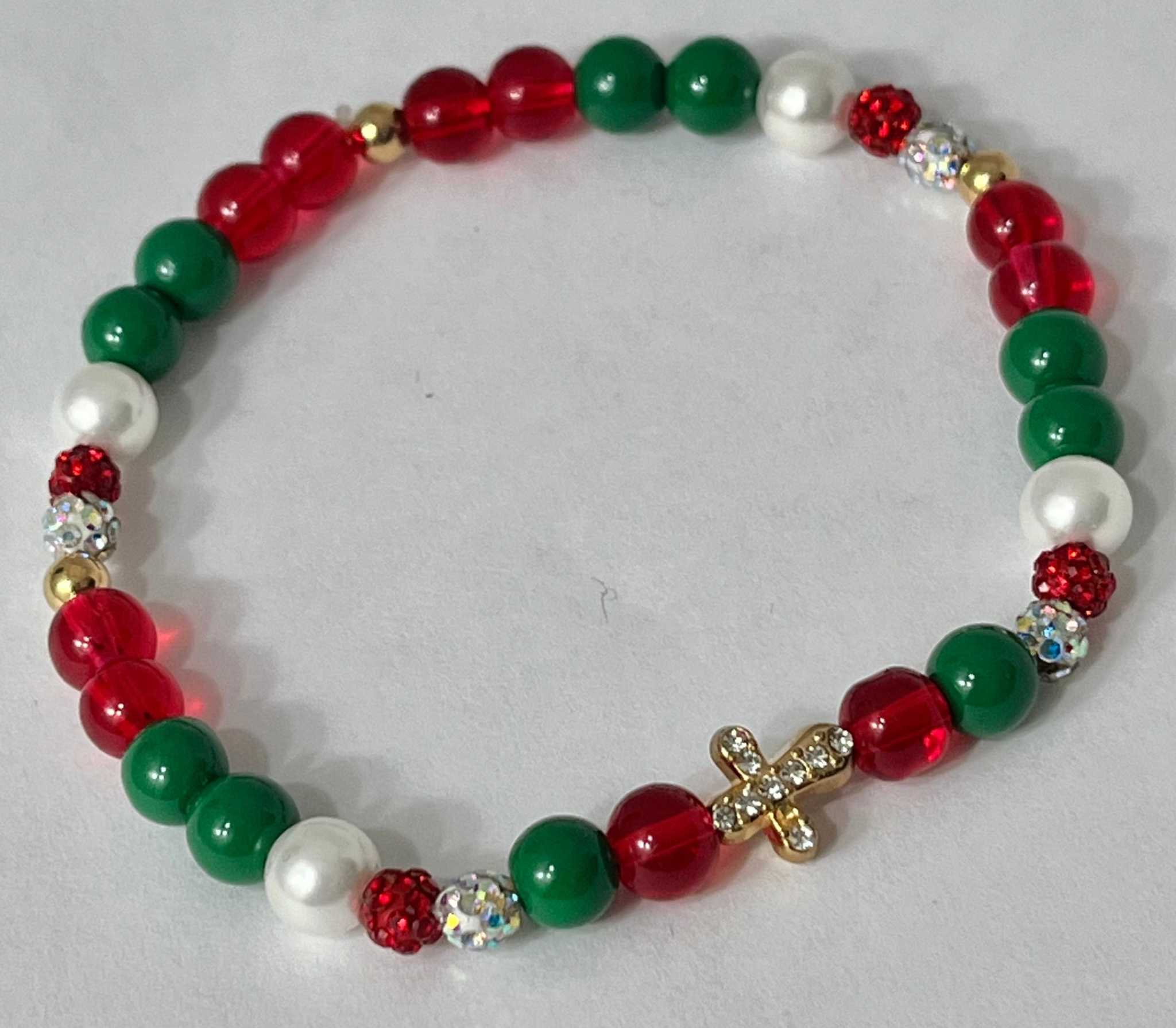 Bead bracelet with red and green beads, white accents, and a gold jeweled cross charm