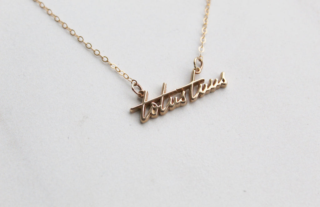 Gold-tone Totus Tuus script pendant on a thin chain