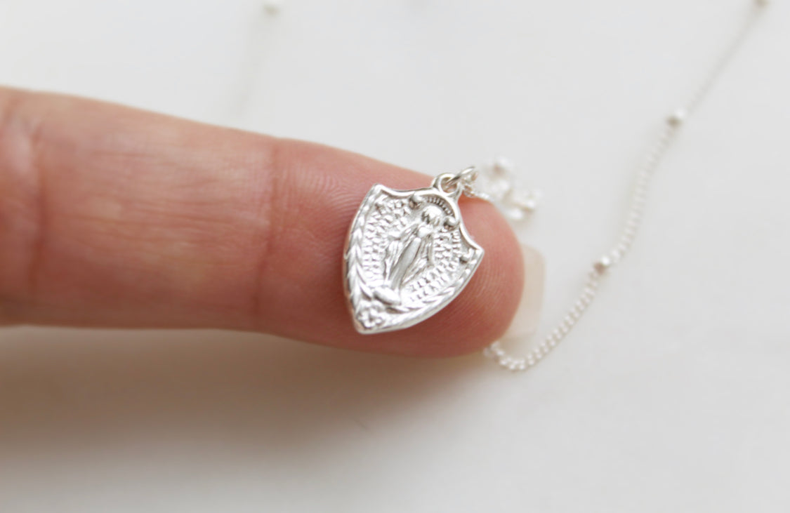 Sterling silver shield pendant with Virgin Mary figure on cable chain, angled close-up