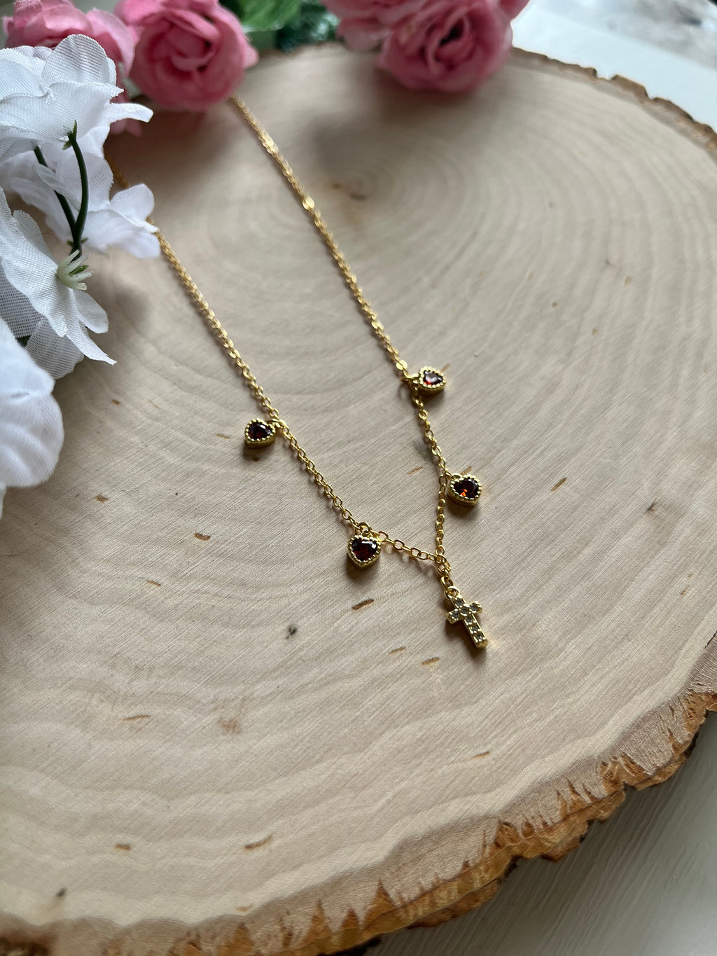 Gold charm necklace close-up with red heart stones and gold cross pendant