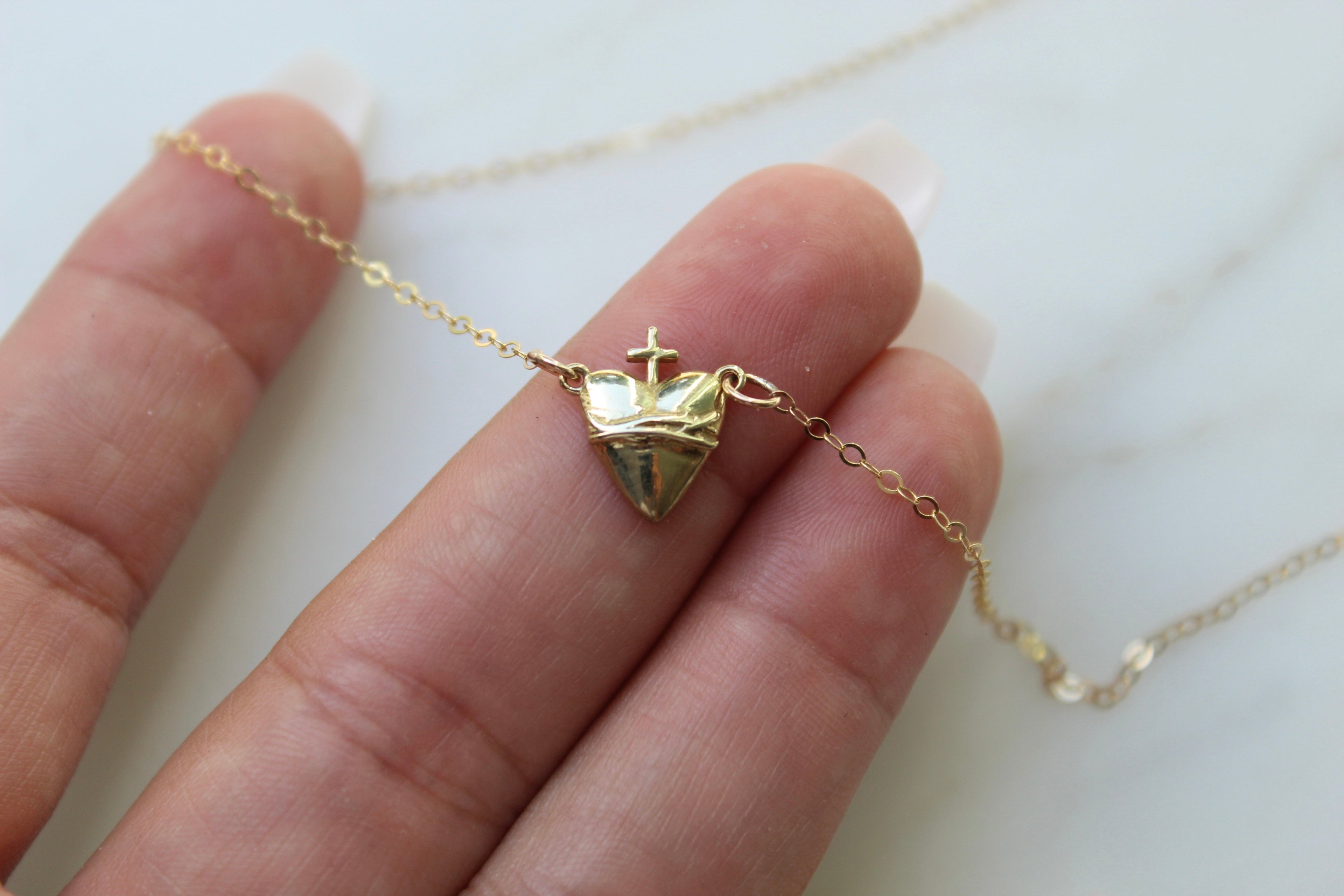 Gold-tone heart pendant necklace with crown and cross charm, shown in hand