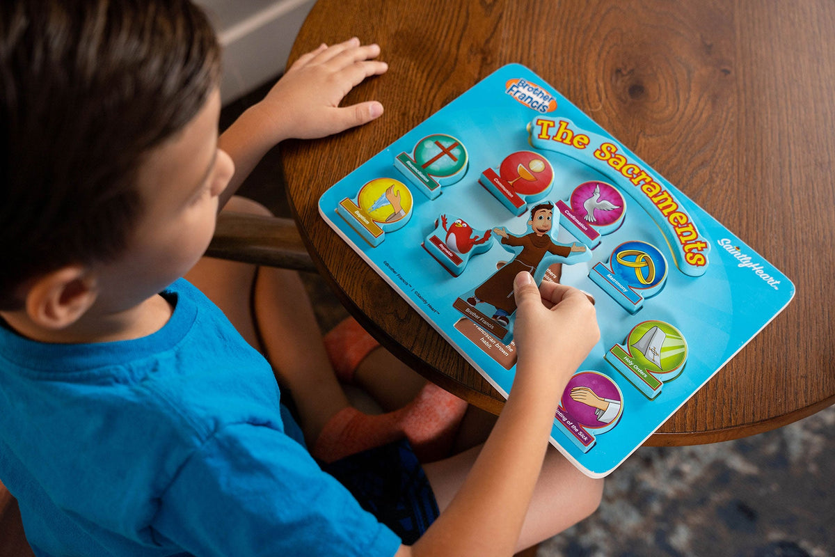 Child playing with blue Sacraments puzzle box showing symbol icons and title