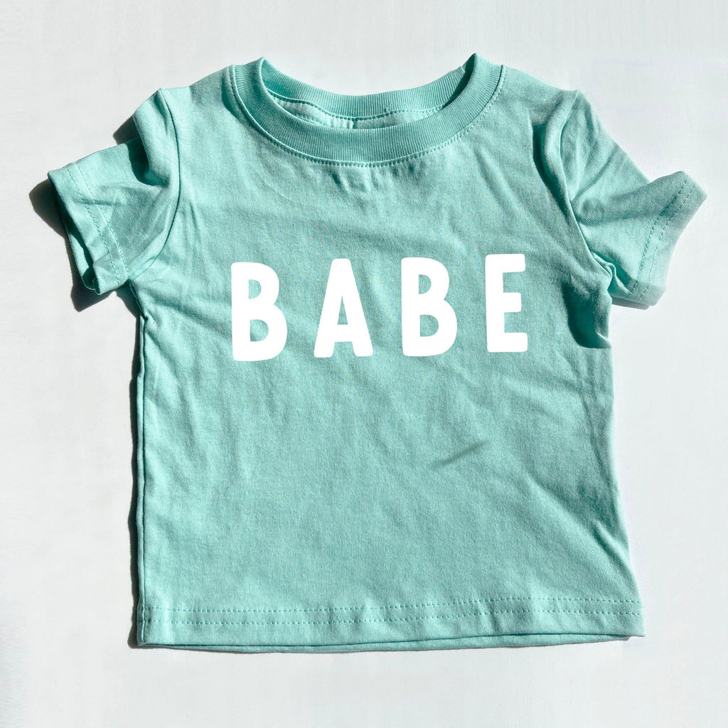 Teal baby T-shirt with white "BABE" rounded-letter print