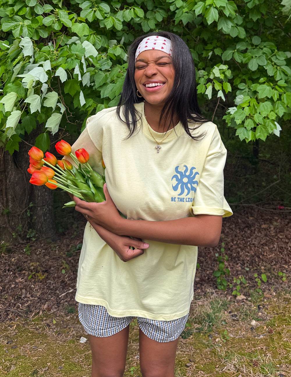 Yellow unisex T-shirt on model, featuring blue sunburst logo and BE THE LIGHT text