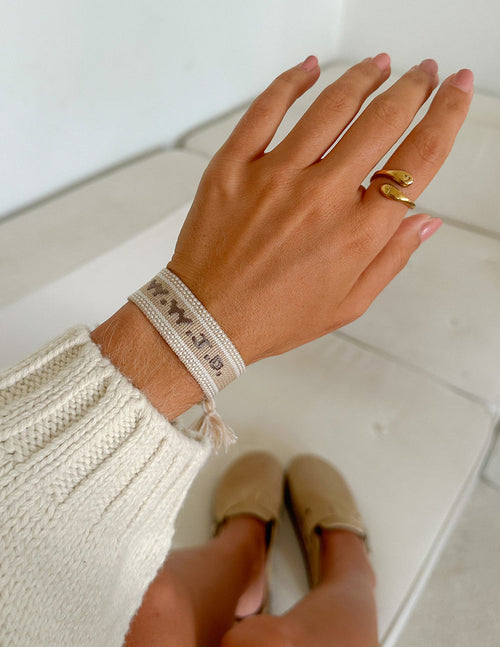 Beige woven bracelet with white embroidery and gold ring clasp on wrist