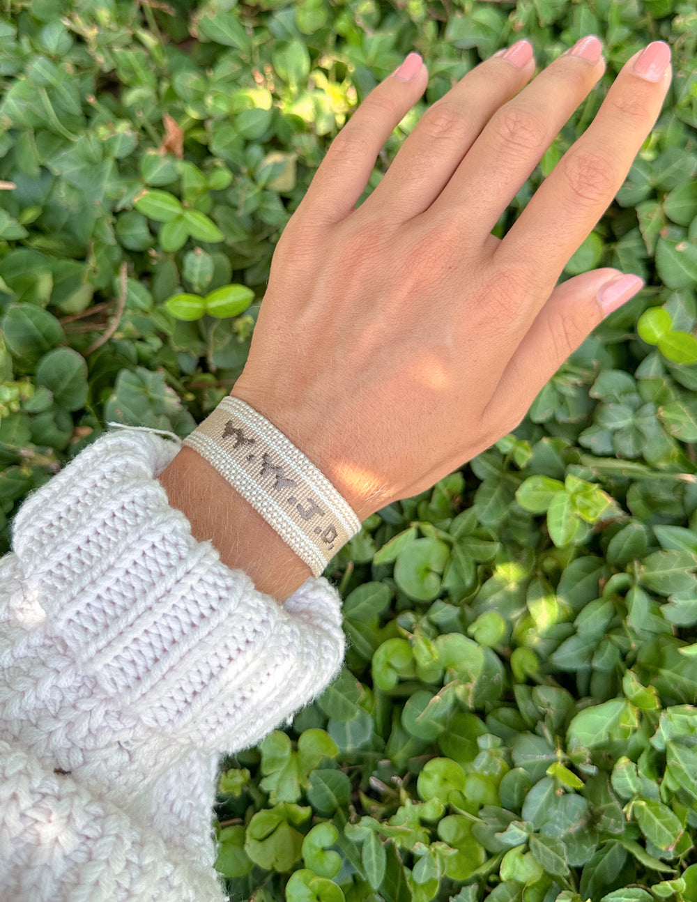 Beige woven bracelet with white motif embroidery and tassel edge on wrist