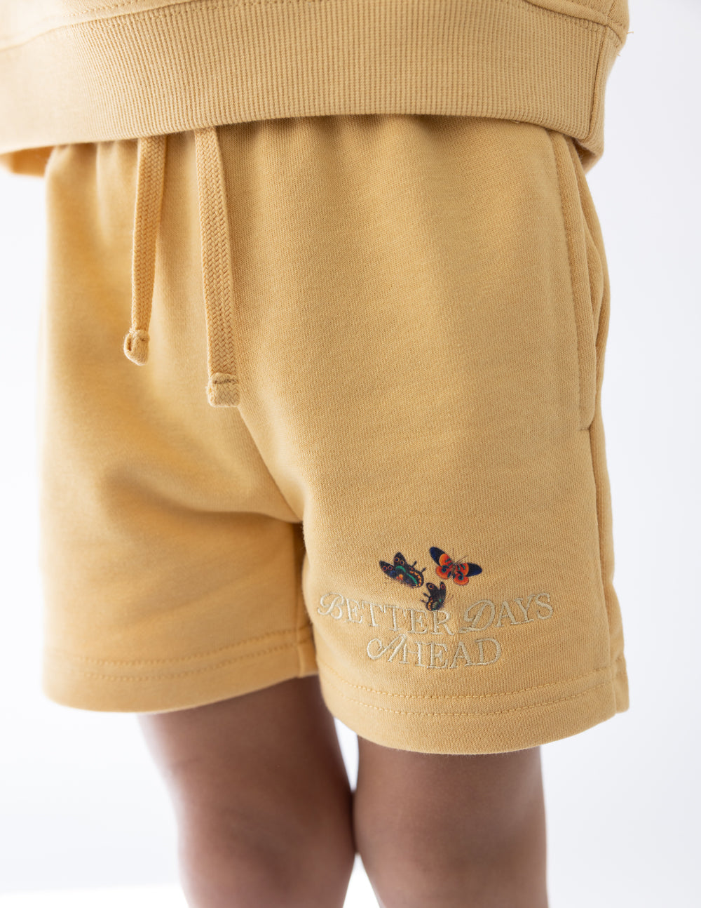 Kids yellow shorts with butterfly graphic on thigh and stitched hem