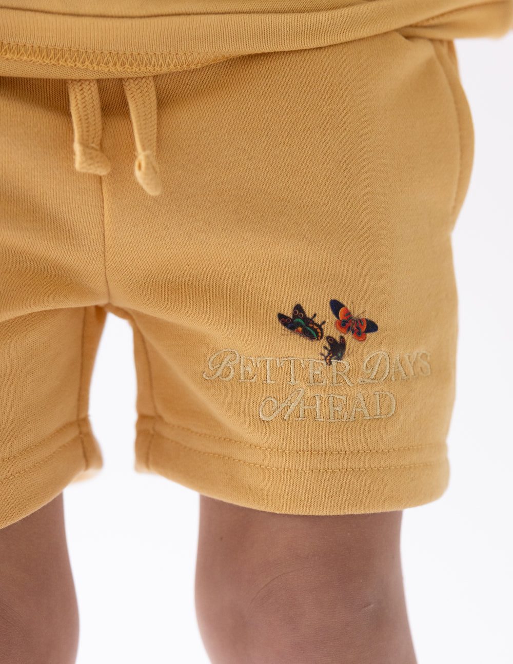 Kids yellow shorts with butterfly graphic and script logo near hem