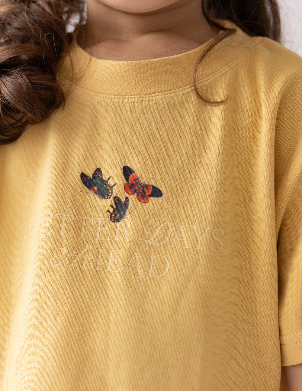 Mustard yellow kids T-shirt with butterflies and faded lettering graphic