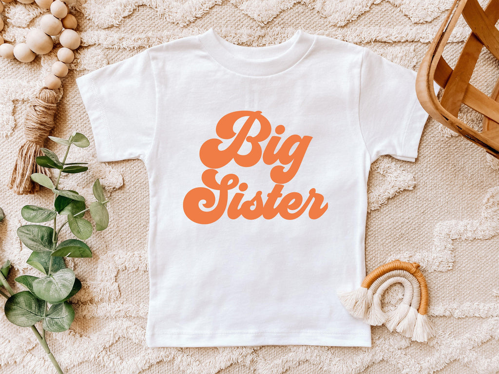White baby T-shirt with orange 'Big Sister' text graphic