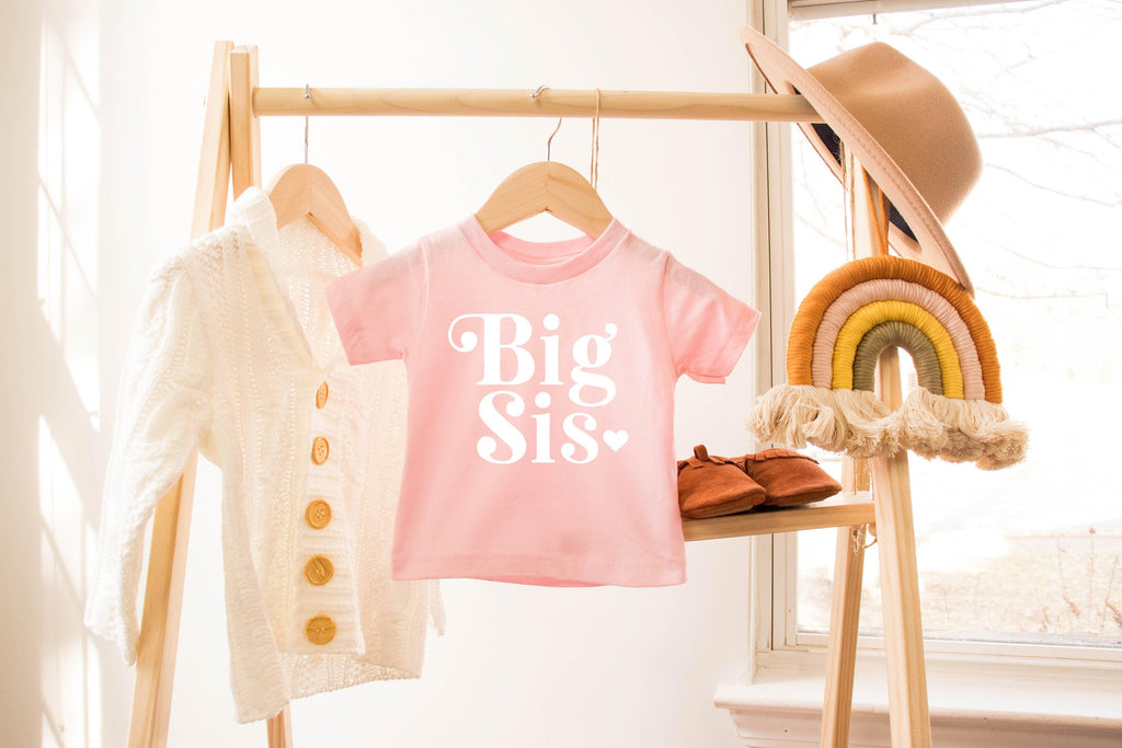 Light pink baby T-shirt with Big Sis heart retro print on a hanger