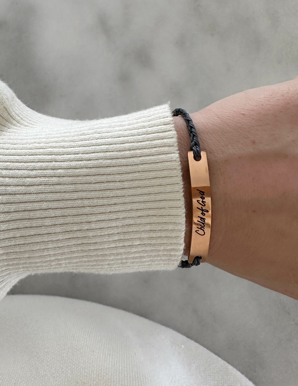 Tan leather bracelet with engraved text and dark adjustable cord on wrist
