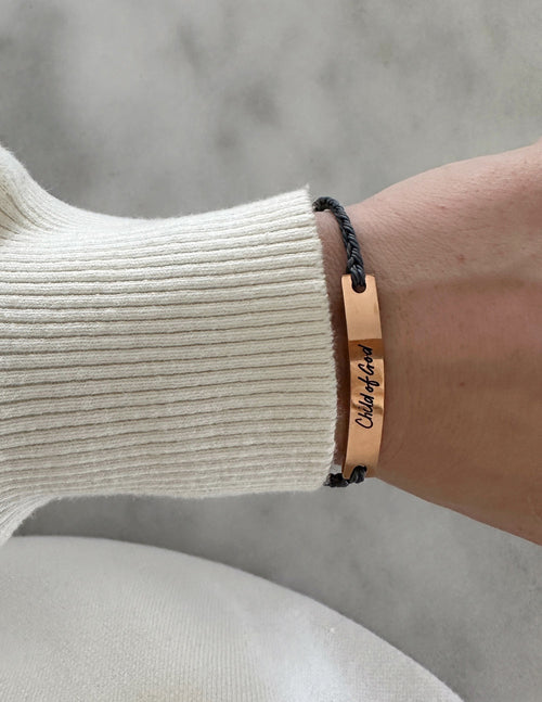 Tan leather bracelet with engraved text and dark adjustable cord on wrist
