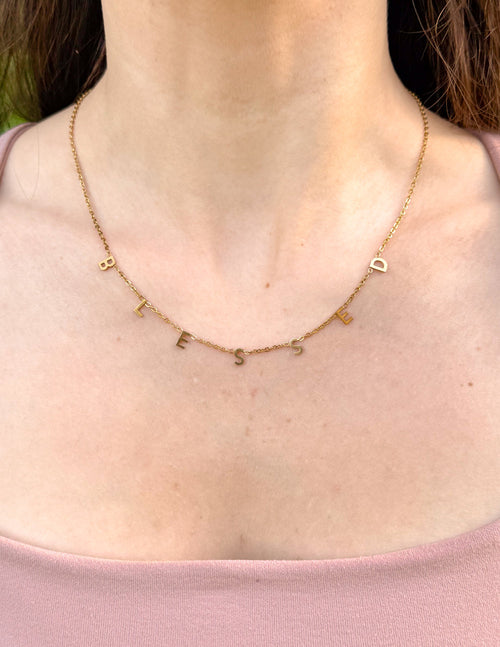 Gold-tone dainty letter-charm necklace resting on the collarbone