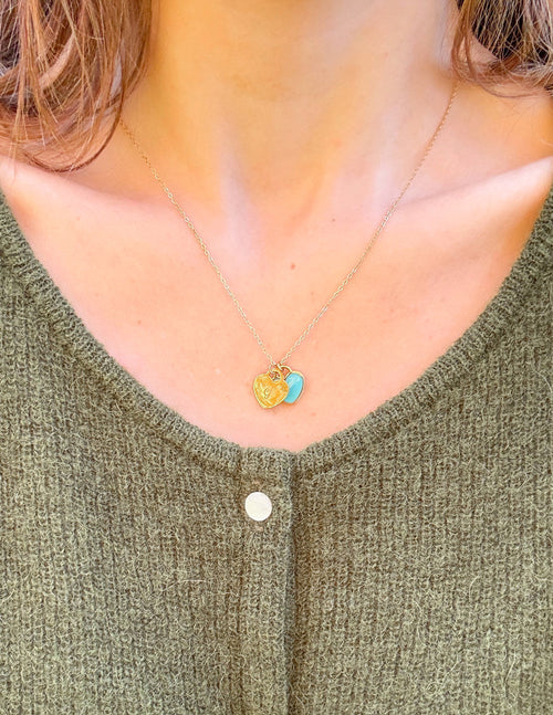 Gold chain necklace with blue enamel heart pendant, worn on neckline