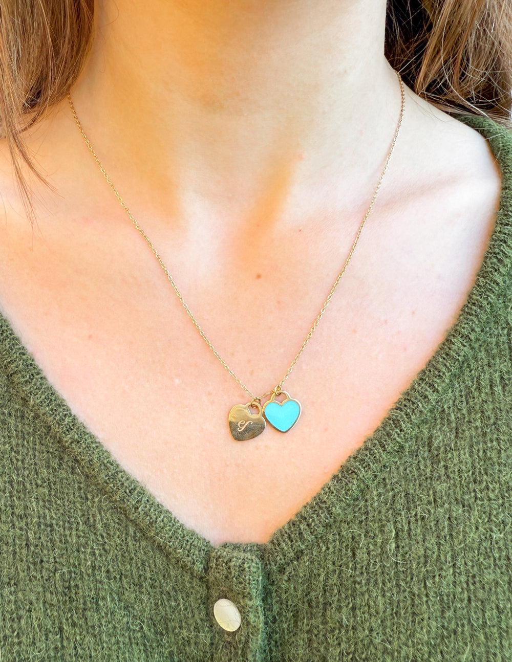 Gold heart logo necklace with blue enamel heart charm, shown at collar
