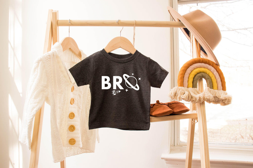 Baby and kids space-themed T-shirts hanging, including black tee with white “BRO” graphic.