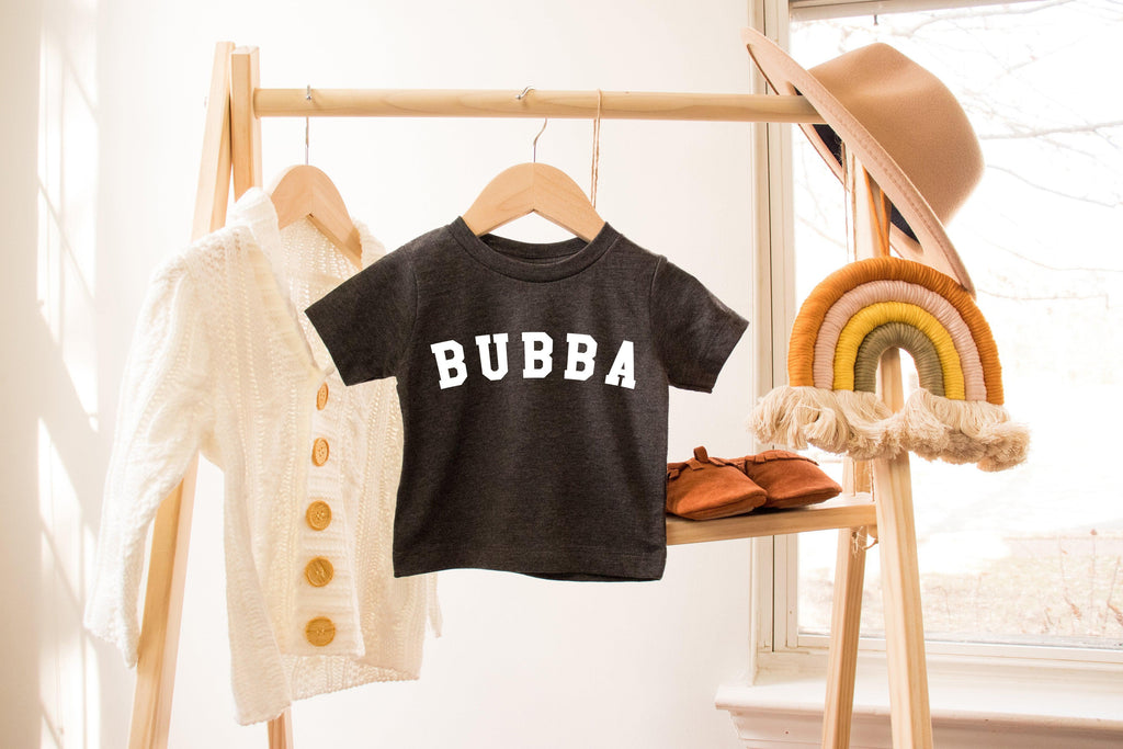 Black toddler T-shirt with white 'BUBBA' lettering, hanging on a rack