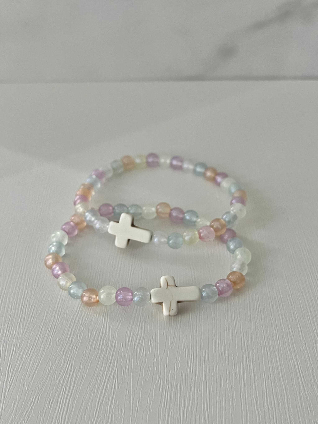 Two pastel beaded bracelets with white cross charms and multicolor beads.