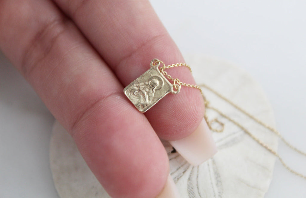 Rectangular scapular charm on gold chain in hand