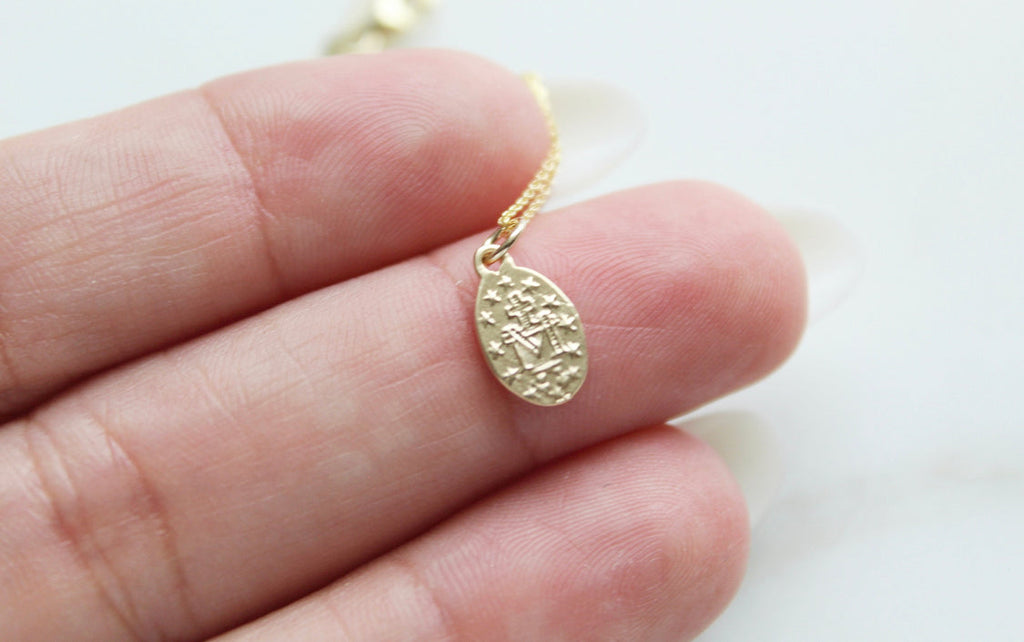 14k gold medal necklace pendant on a thin chain held in a hand, close-up