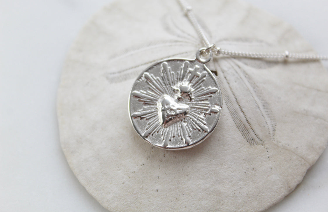 Silver round sacred heart coin pendant charm on fine chain, close-up view.