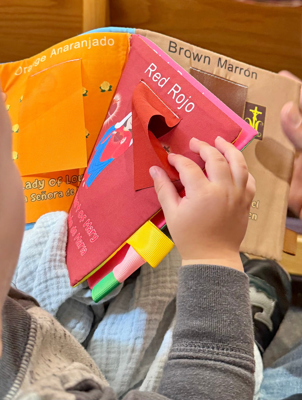 Child’s hands holding fabric Mary colors books: orange, brown, and red page covers.