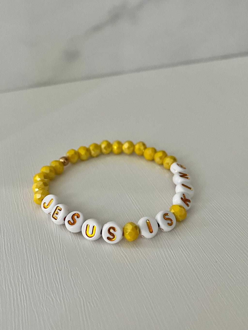 Bead bracelet with yellow round beads and white letter beads reading JESUS IS KING