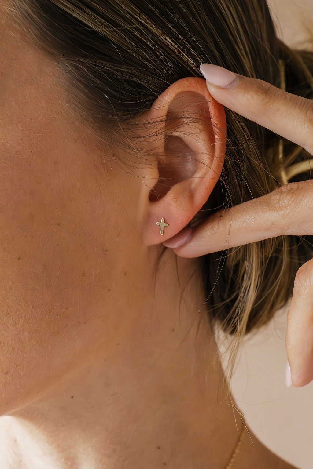 Gold-tone cross stud earring on a visible ear, close-up view.