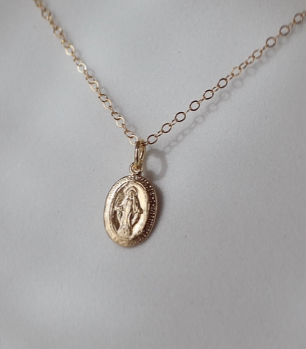 Close-up of gold-tone oval medal pendant necklace on a chain
