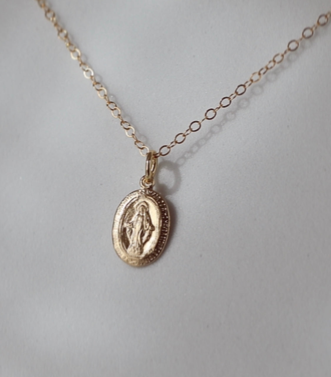 Close-up of gold-tone oval medal pendant necklace on a chain