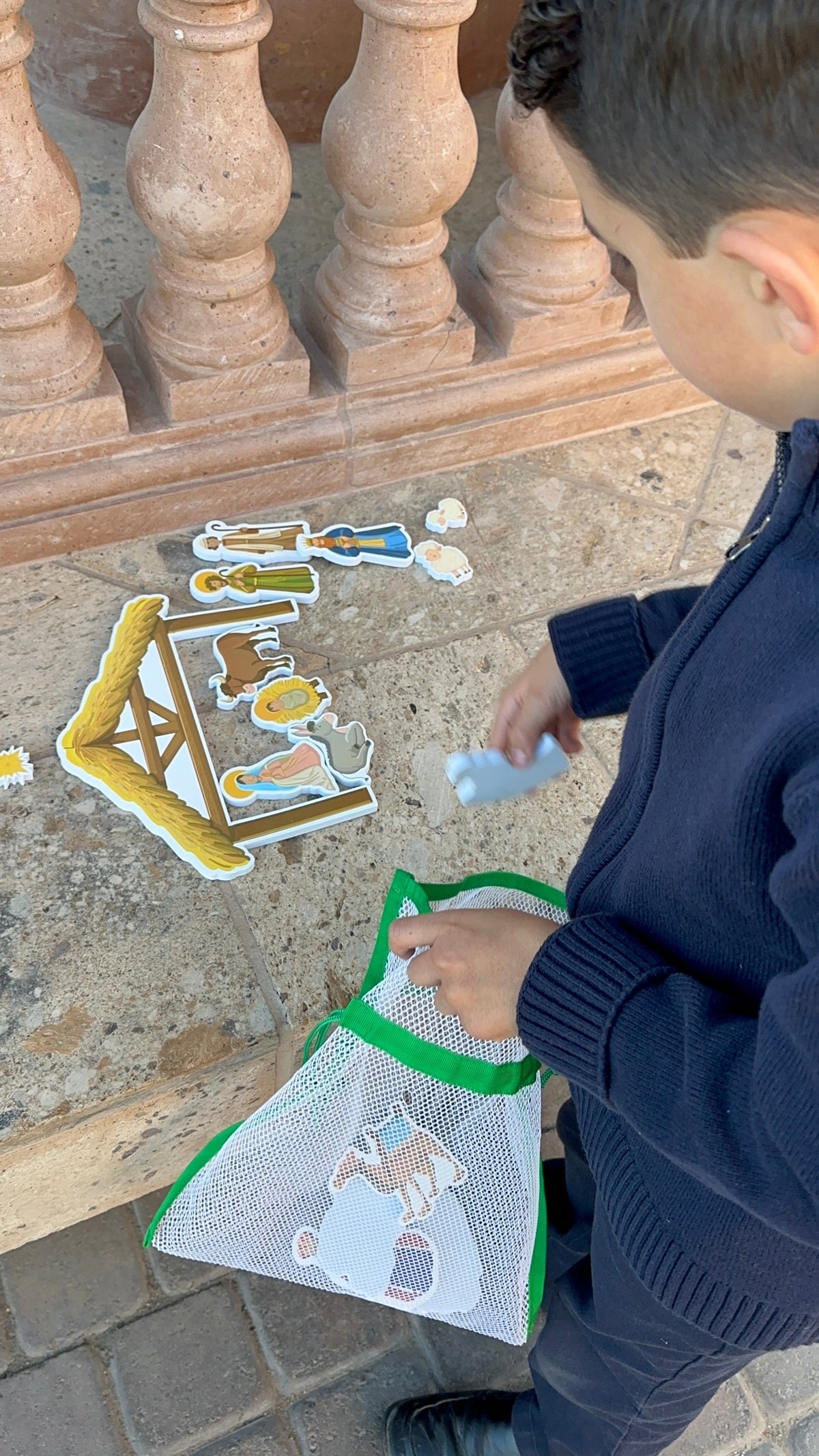 Child playing with nativity bath toy cutouts on a patio floor