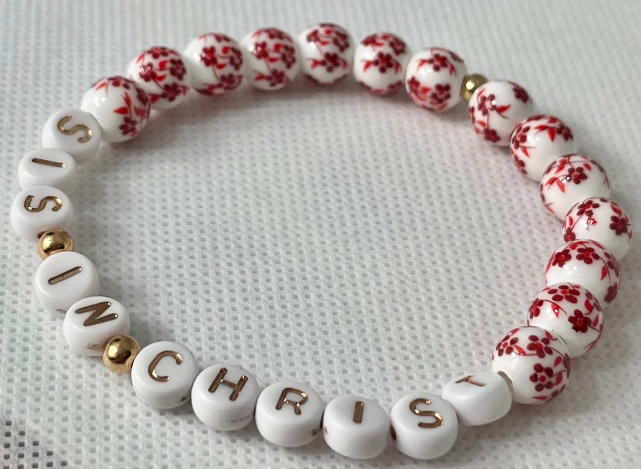 Red bead bracelet with white letter beads spelling IN CHRIST and red floral beads