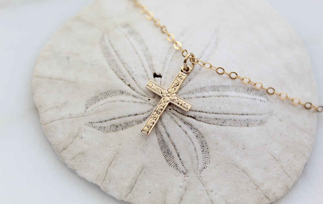 Gold cross pendant necklace with chain on shell, angled cross view