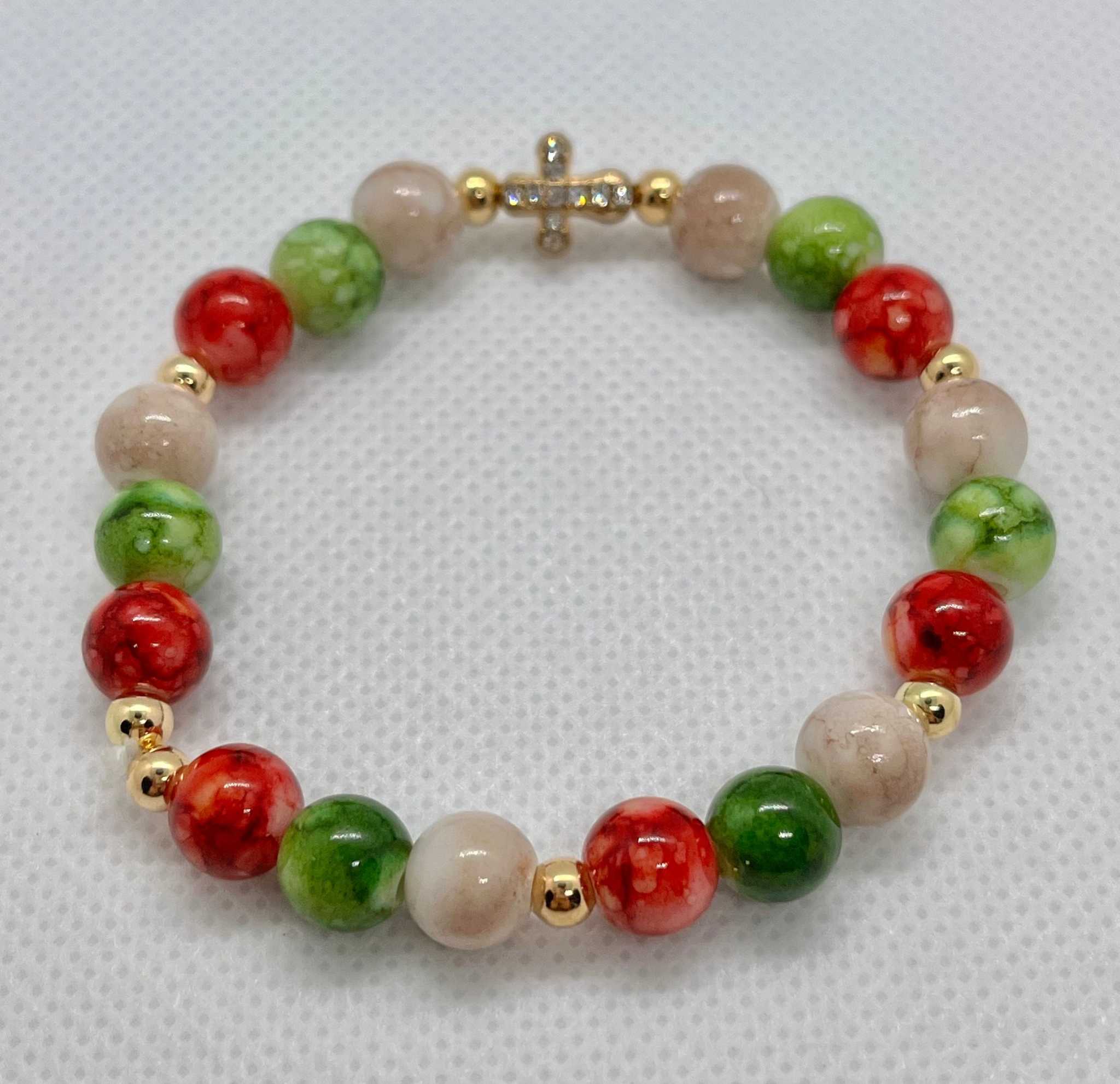 Bead bracelet with marbled beige beads, green and red accents, and a gold jeweled cross