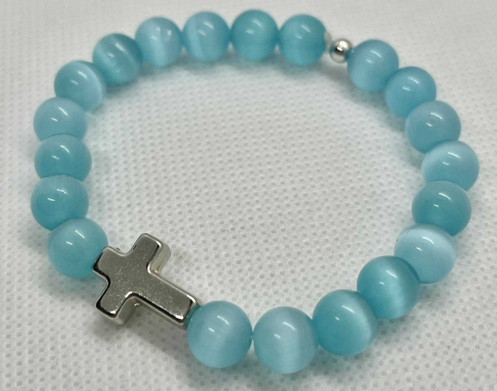 Blue-green beaded cross bracelet with silver cross charm, close-up view.
