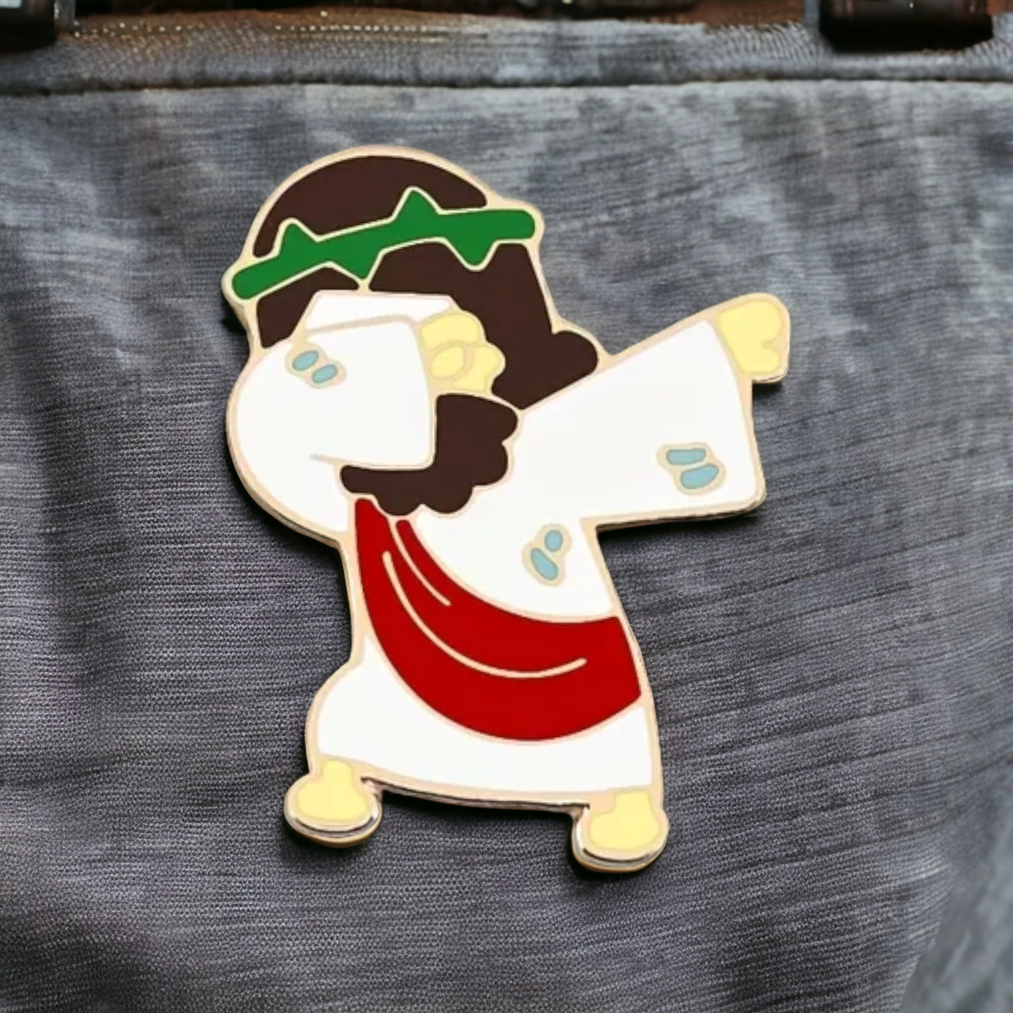 Jesus dabbing enamel pin, gold-tone outline; white arms, red robe, green head wrap