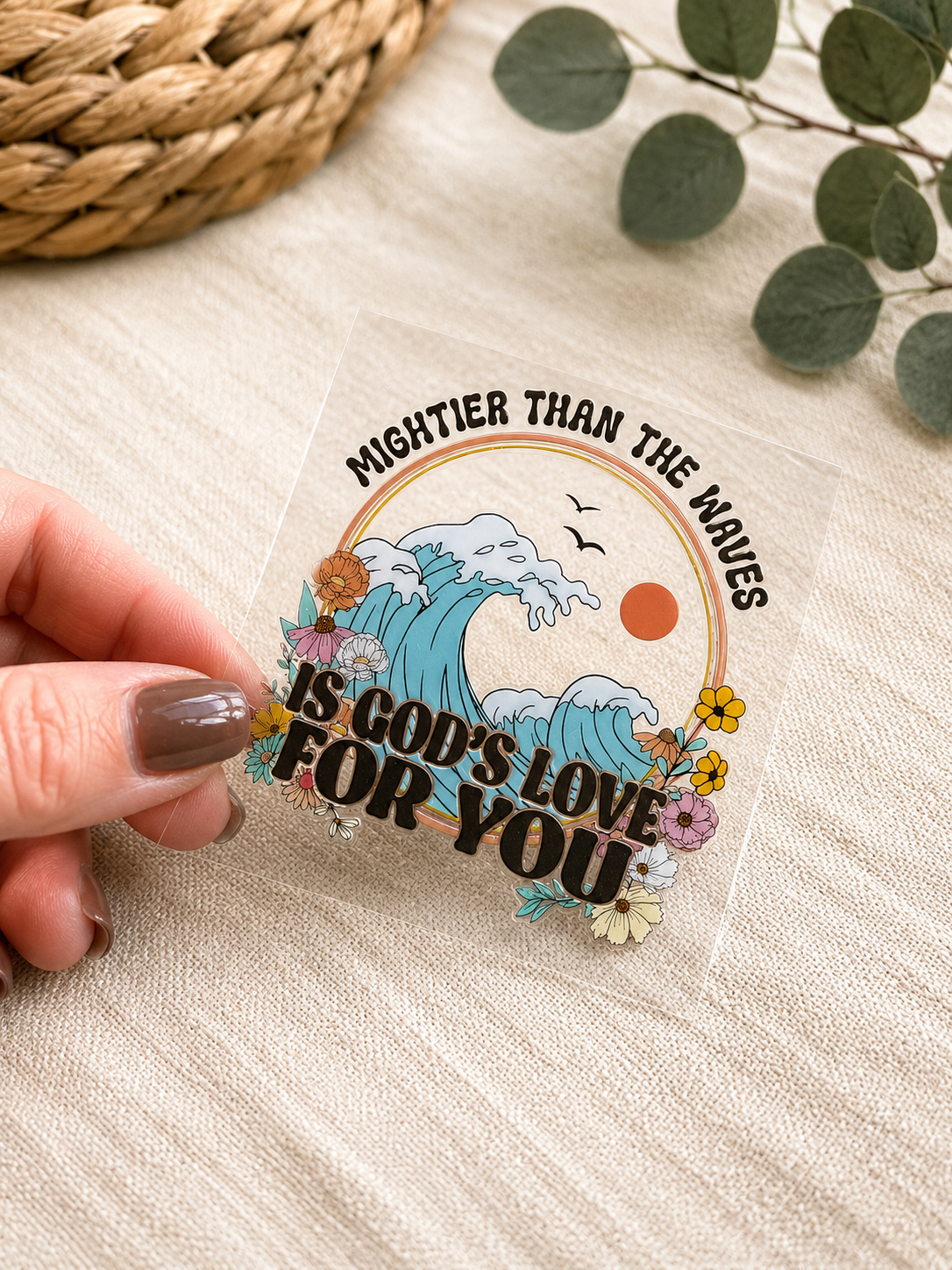 UVDTF decal with ocean wave illustration and floral lettering, held in fingers