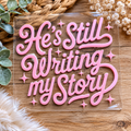 UV DTF decal with pink script 'He's Still Writing My Story' and star sparkles
