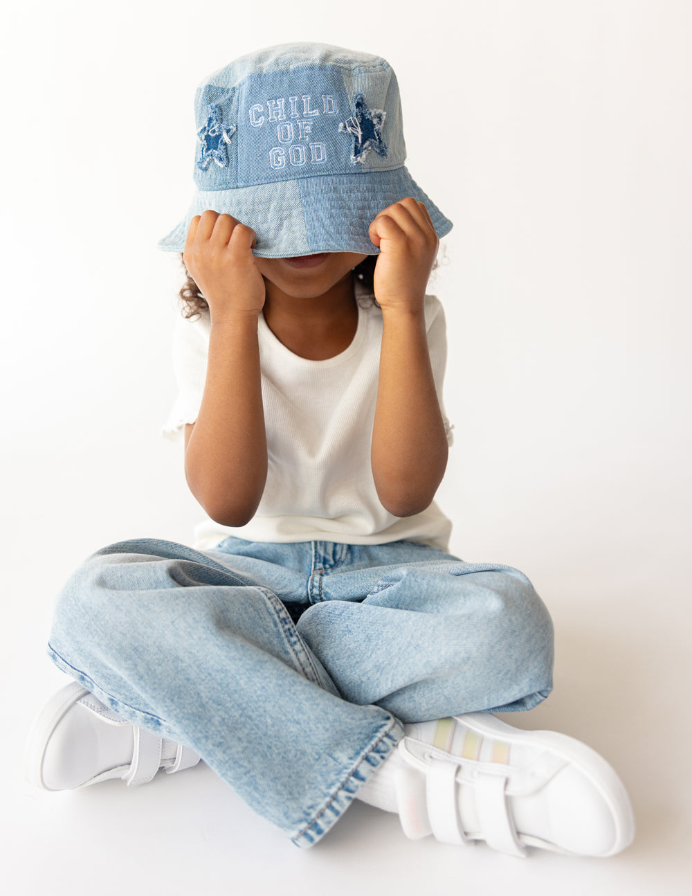 Light blue denim kids bucket hat worn by child, showing front 'CHILD OF GOD' logo