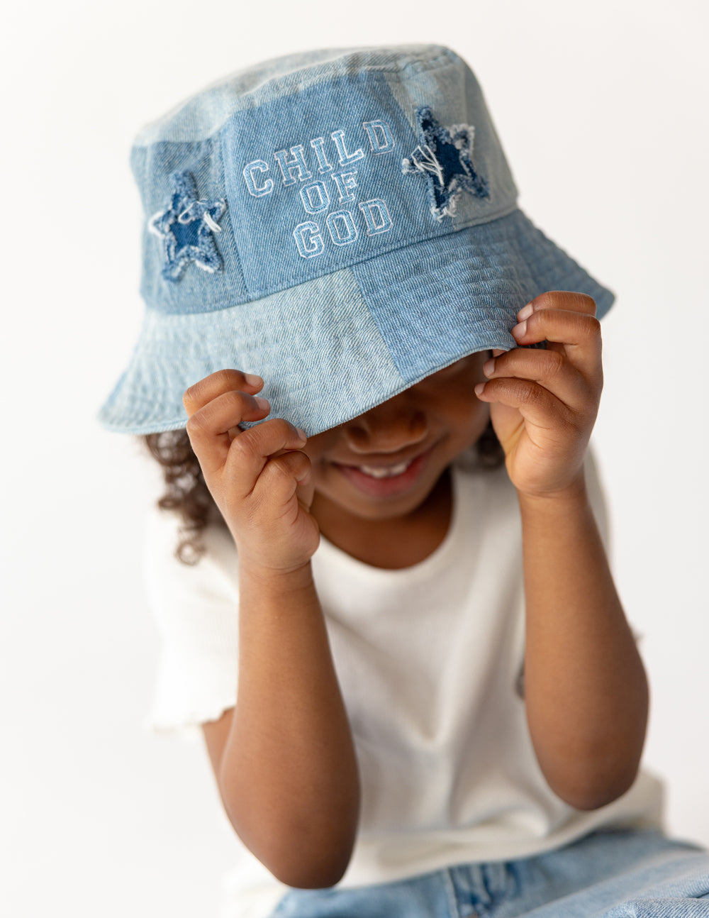 Light blue denim kids bucket hat worn, showing 'CHILD OF GOD' front and star