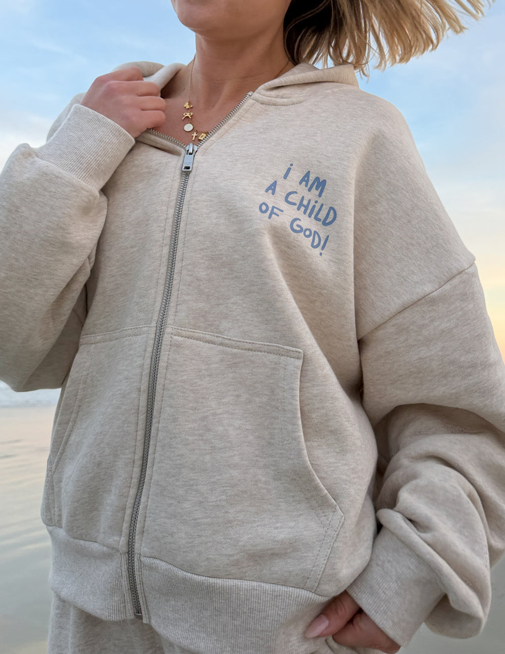 Light beige full-zip hoodie with hood, front pocket, and graphic text