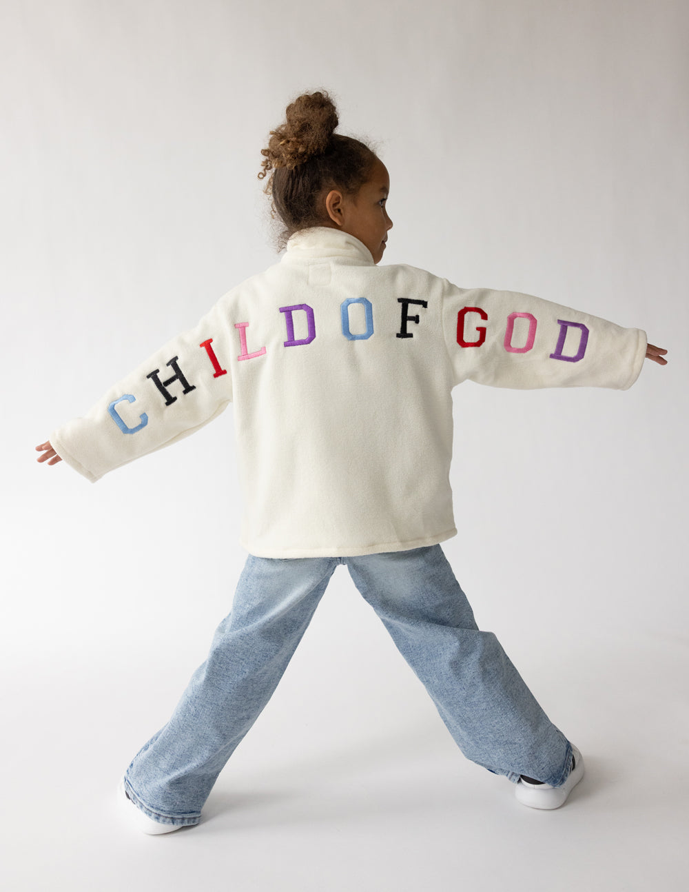 Kids cream fleece pullover with multicolor “CHILD OF GOD” logo across back