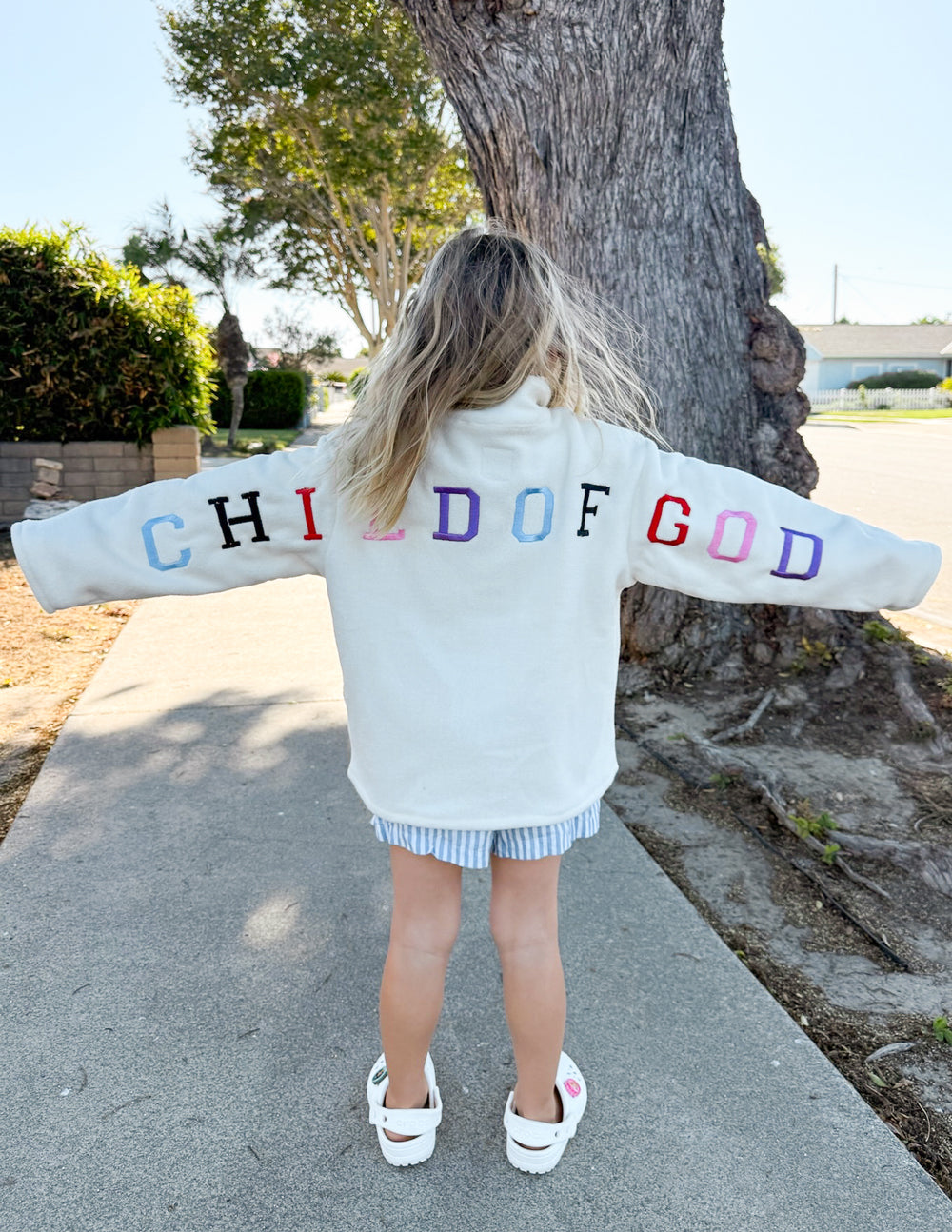 Kids cream fleece pullover with multicolor “CHILD OF GOD” logo on back