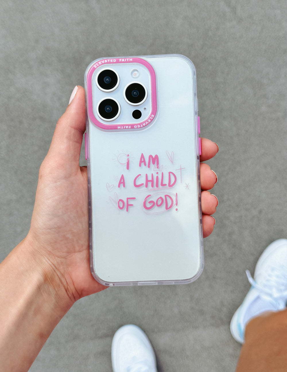 Hand holding pink clear phone case with 'I AM A CHILD OF GOD!' text and cutouts