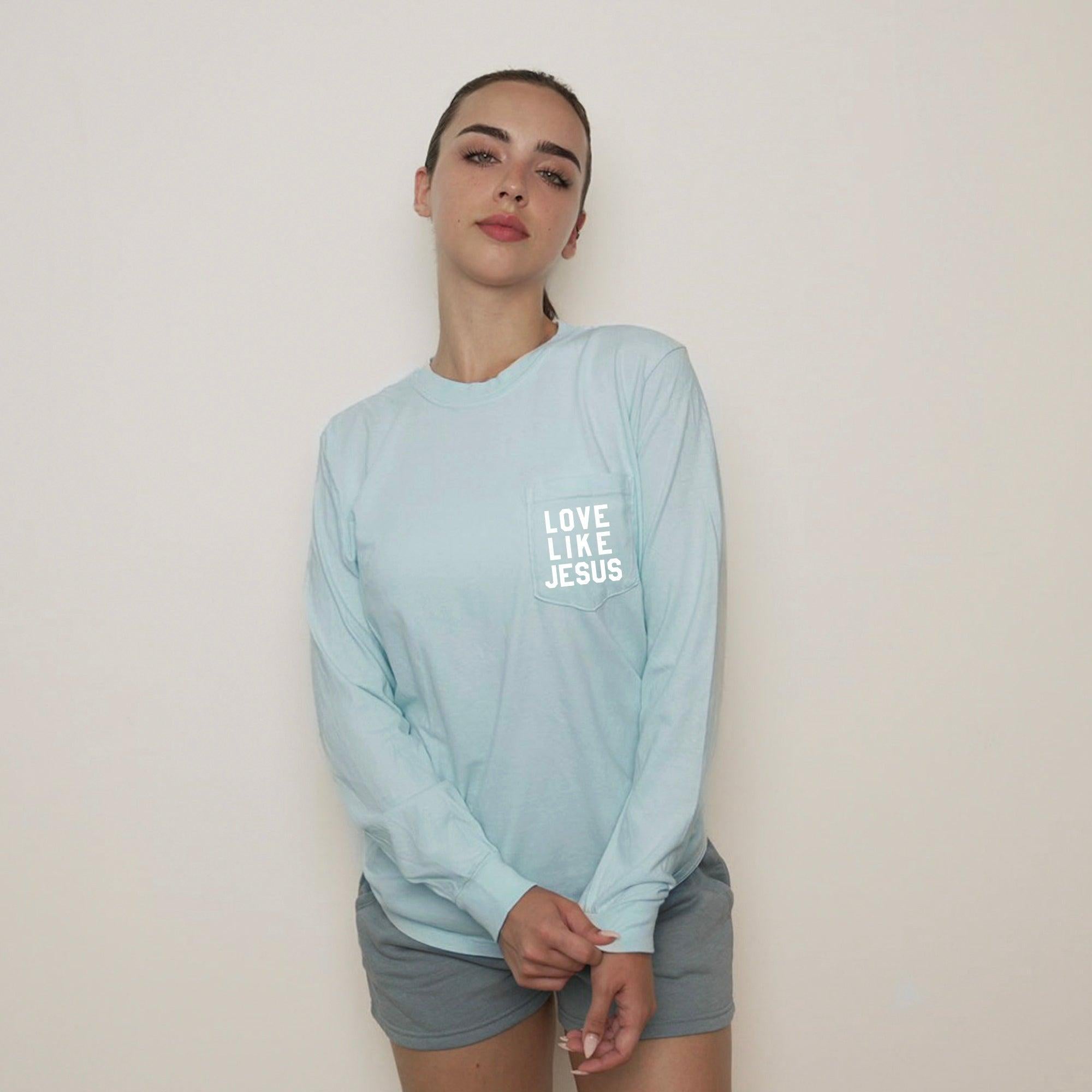 Light blue long sleeve pocket tee with "LOVE LIKE JESUS" chest print