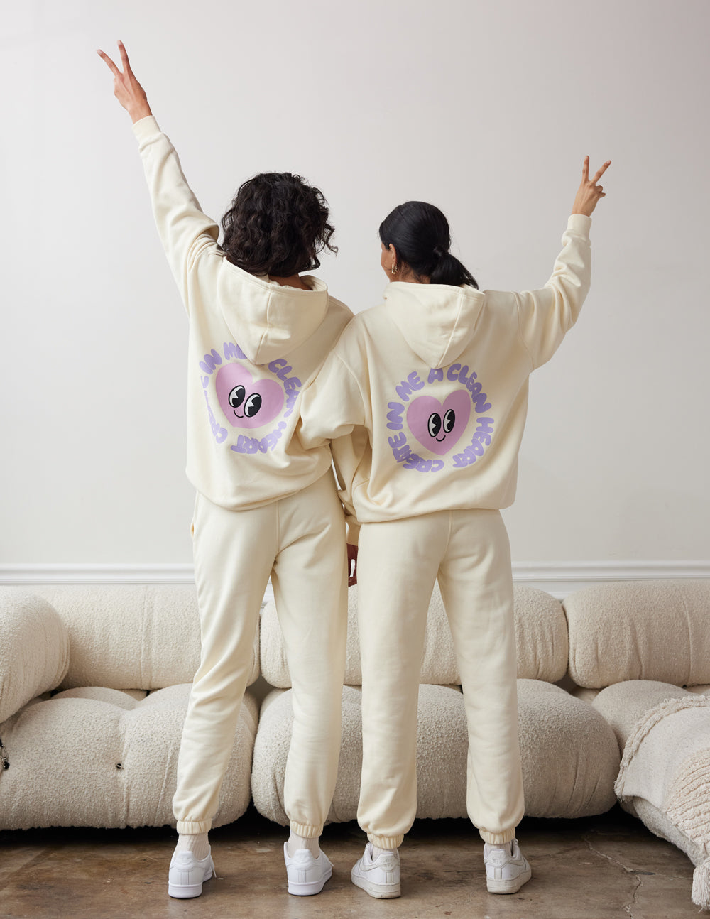 Unisex cream hoodie with purple alien-face back graphic, two-person view