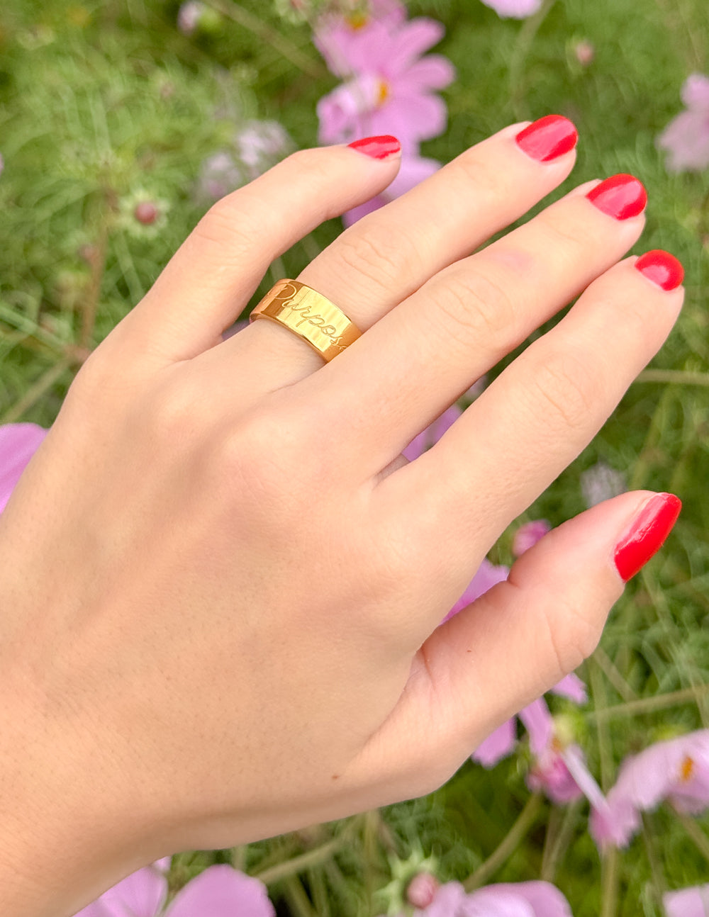 Gold band ring with engraved face on hand with red nail polish