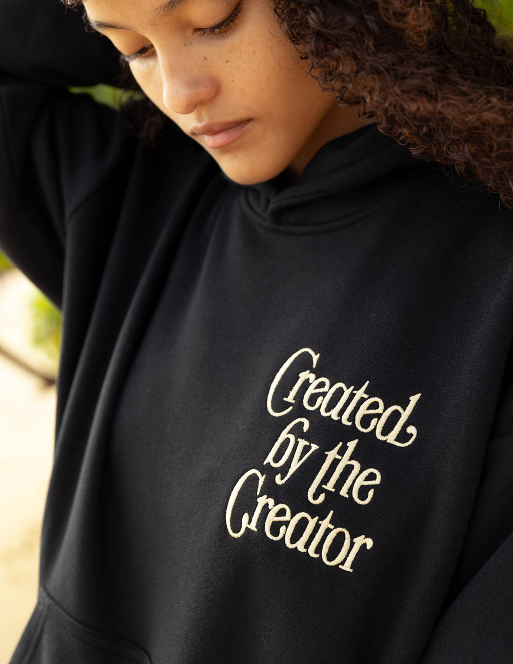 Black unisex hoodie close-up of chest logo: 'Created by the Creator'